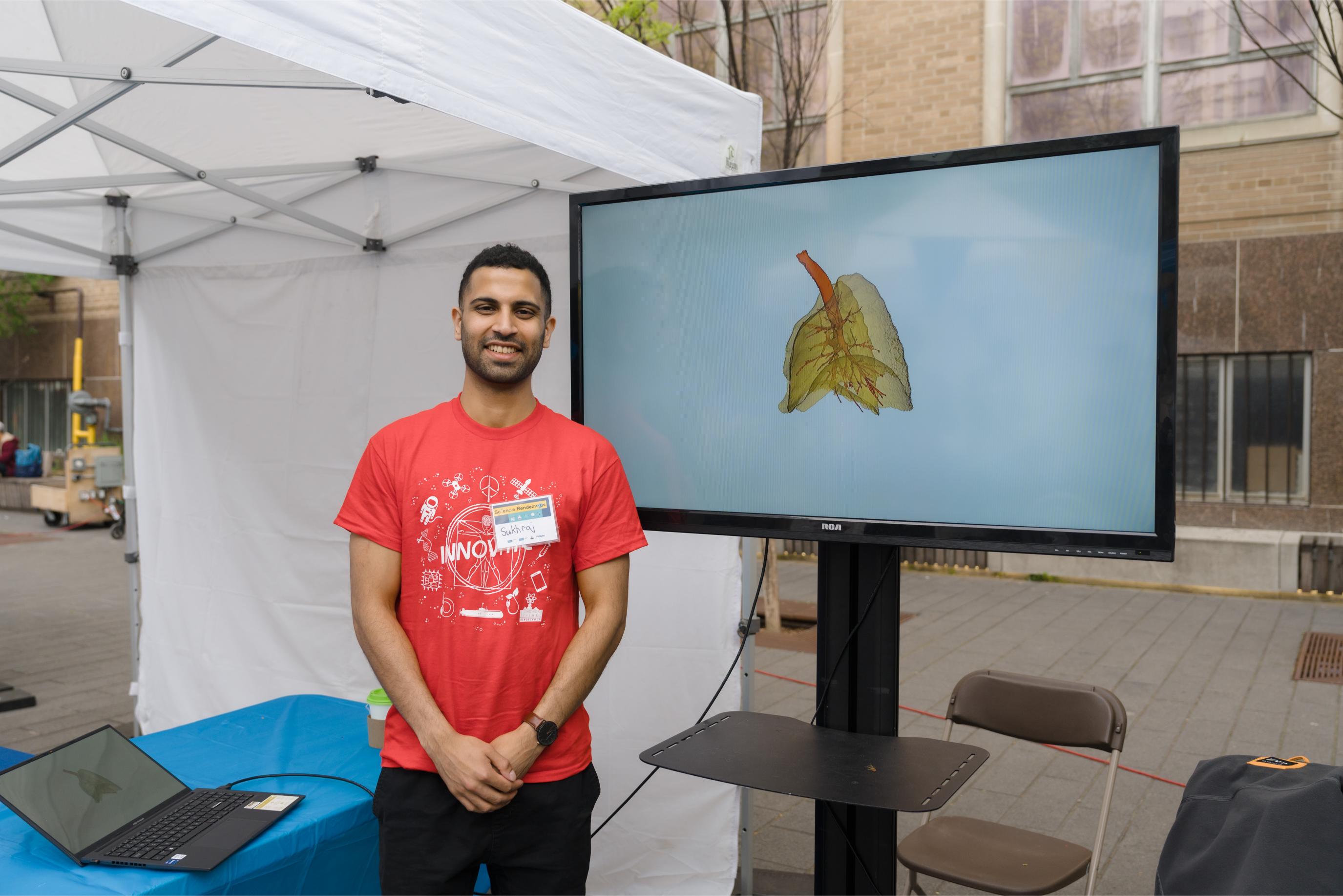 A volunteer standing in front of a TV screen which showcases a 3D model of the human lung at the Lung Function Booth.